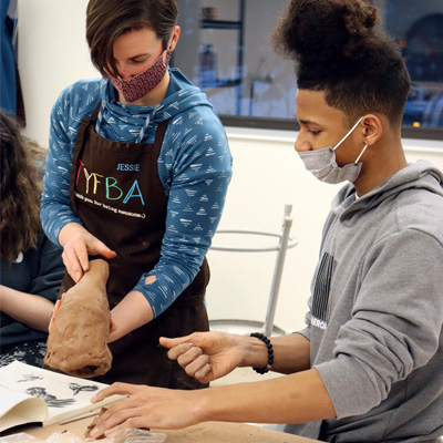 An ECAT arts instructor holds a clay sculpture next to her student.